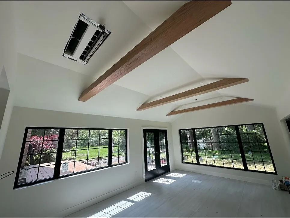 Freshly painted vaulted sunroom with warm wood ceiling beams, black-grid windows, and a garden view — a completed Crotti's Painting interior.